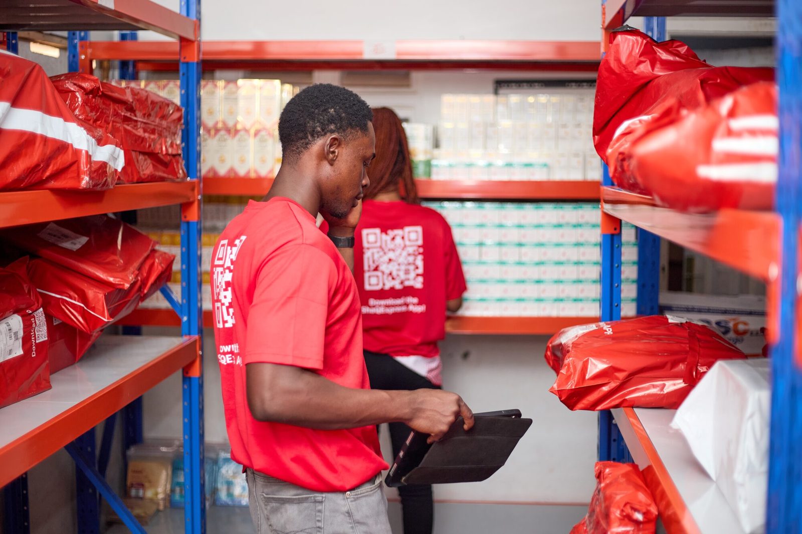 ShaQ Express staff checking stock on warehouse shelves with a tablet